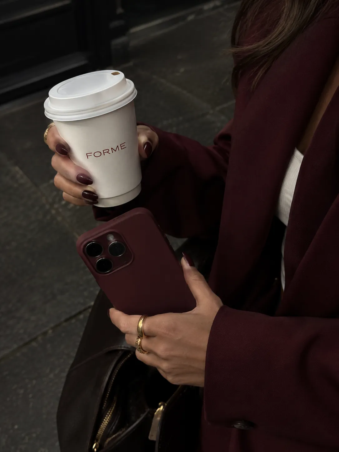 Hands holding a FORME coffee cup and a burgundy phone