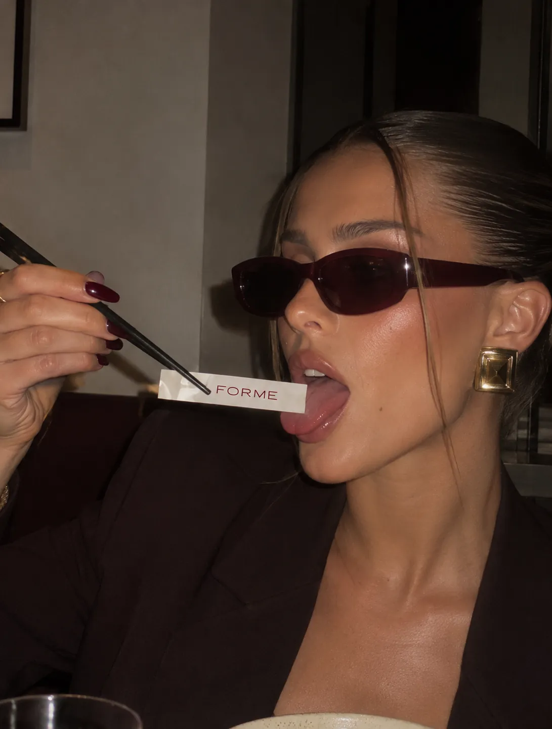 A woman in dark sunglasses holding chopsticks with a FORME wrapper