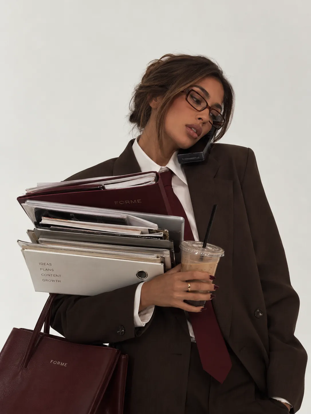 A woman on the phone carrying FORME folders marked ideas, plans, content, growth